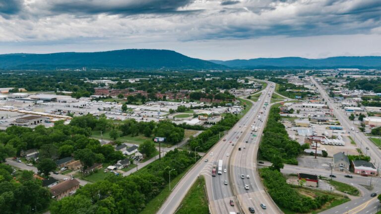 Aerial view of a busy highway in Chattanooga with lush greenery and urban landscape under cloudy skies.